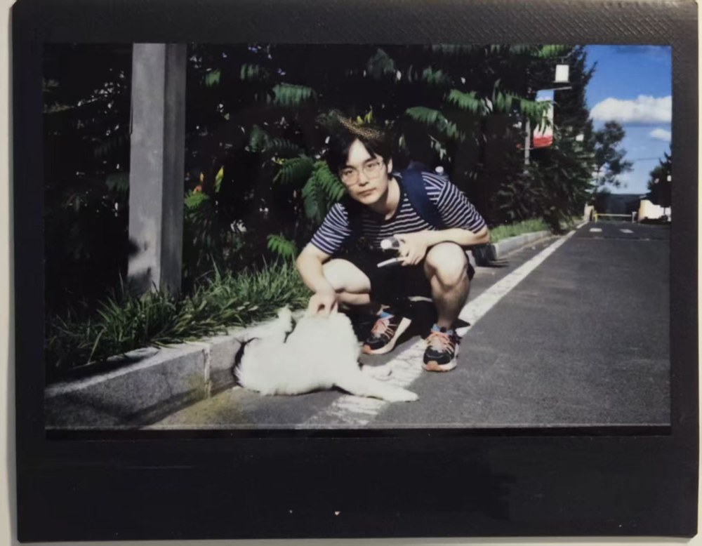 William crouching beside a small white dog outdoors, in a framed snapshot